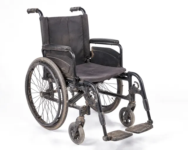 A manual wheelchair before cleaning, with dulled paintwork and dust across the frame and wheels.