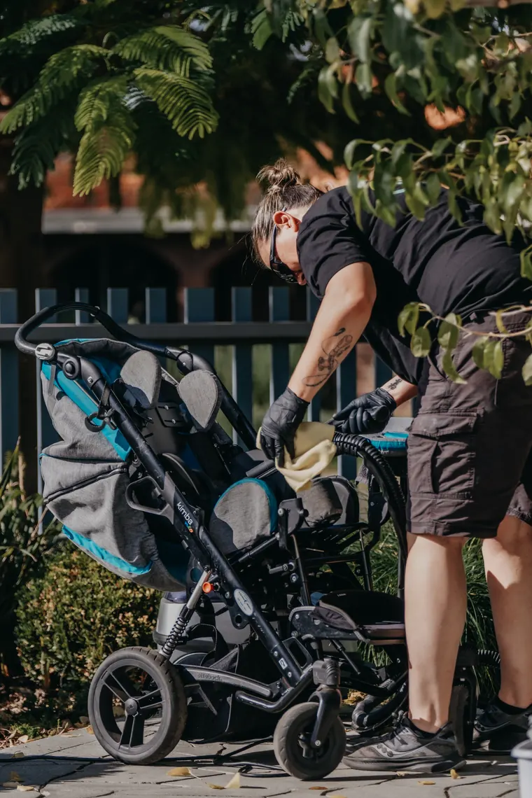 A Wheely Clean Mobility technician cleaning a paediatric mobility buggy outdoors at a client&rsquo;s home in Perth.