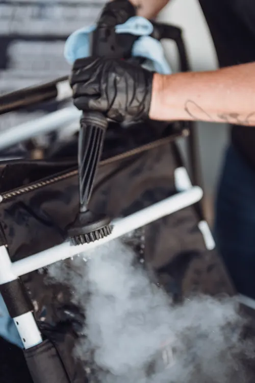 A gloved hand working a detail brush along a wheelchair frame.