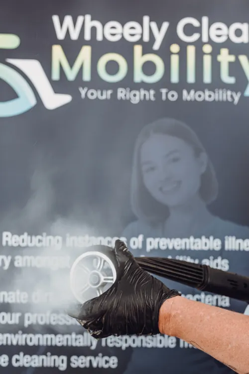 A castor wheel being steam cleaned in front of the Wheely Clean Mobility banner.