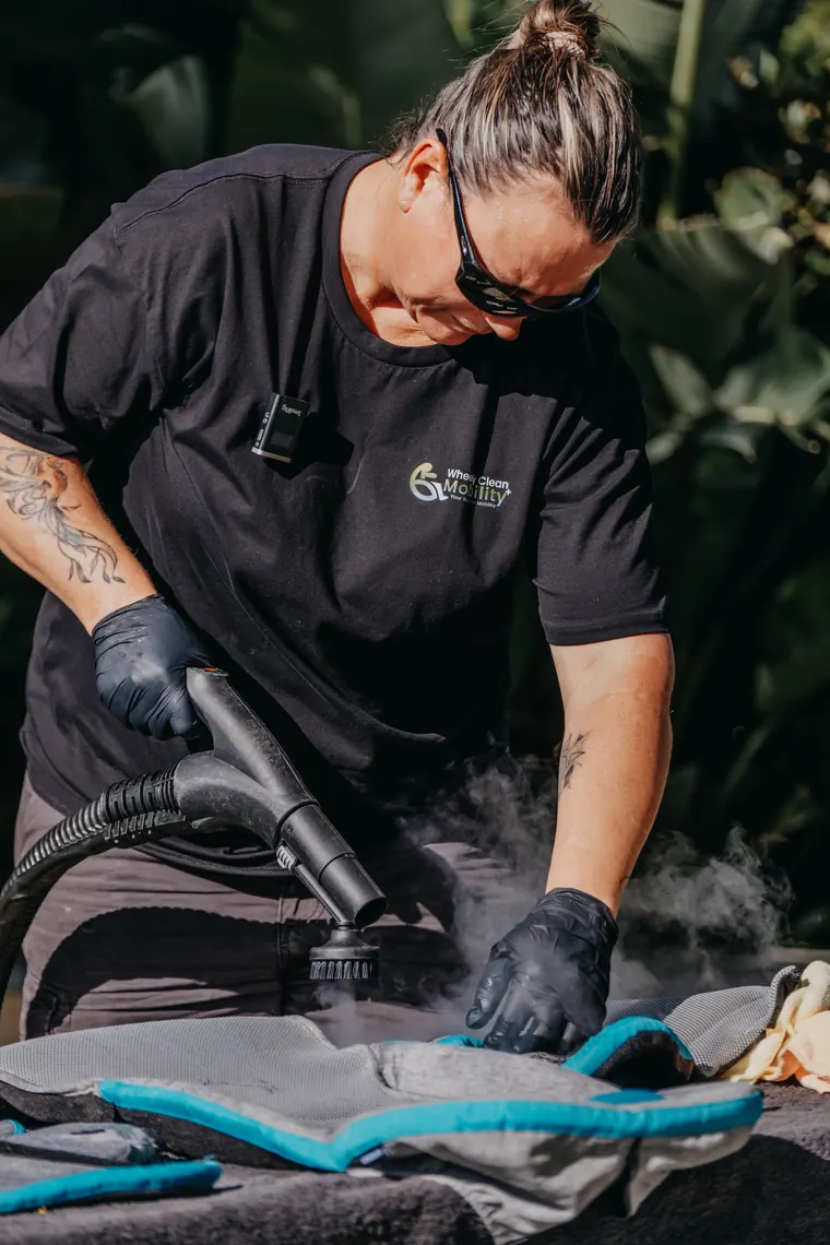 A Wheely Clean Mobility technician steam cleaning a wheelchair seat cushion outdoors.