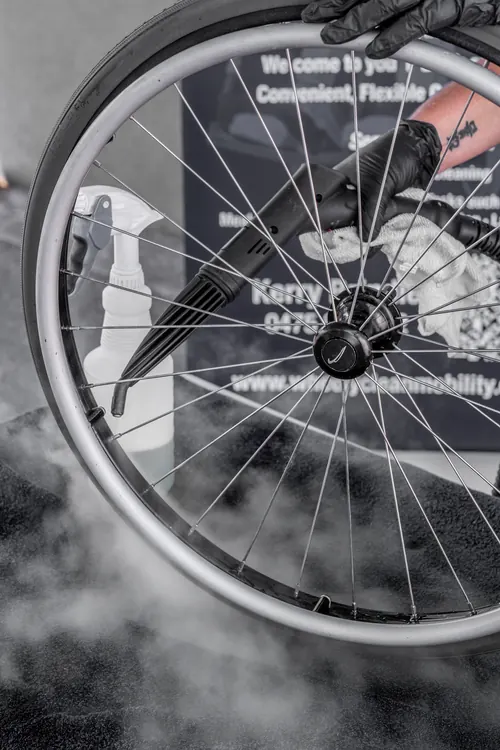 Steam cleaning the spokes and rim of a wheelchair rear wheel.